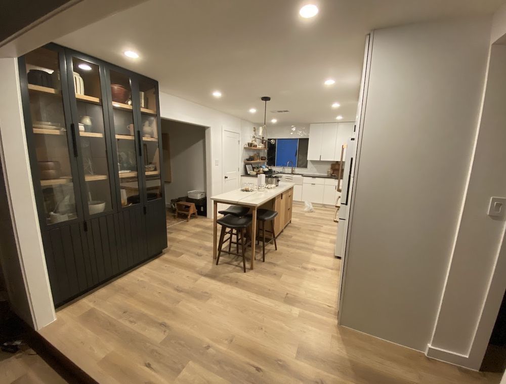 Modern kitchen with wood floors, island with stools, built-in glass front cabinet.