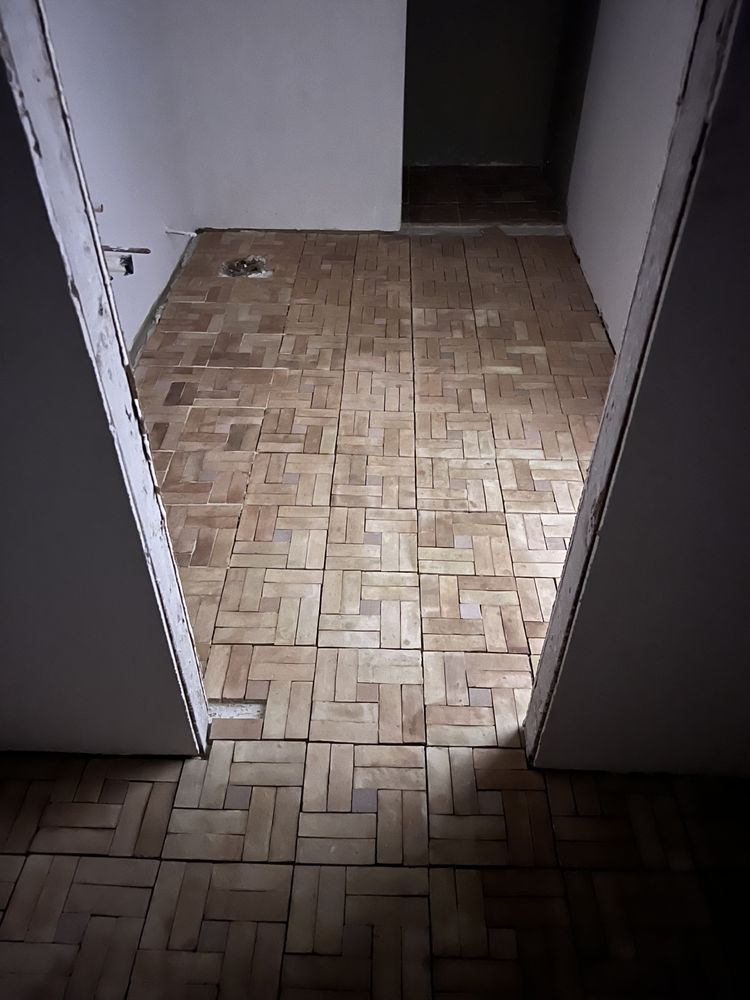 Hallway with light brown parquet flooring, lit by sunlight, between two white walls with door frames.