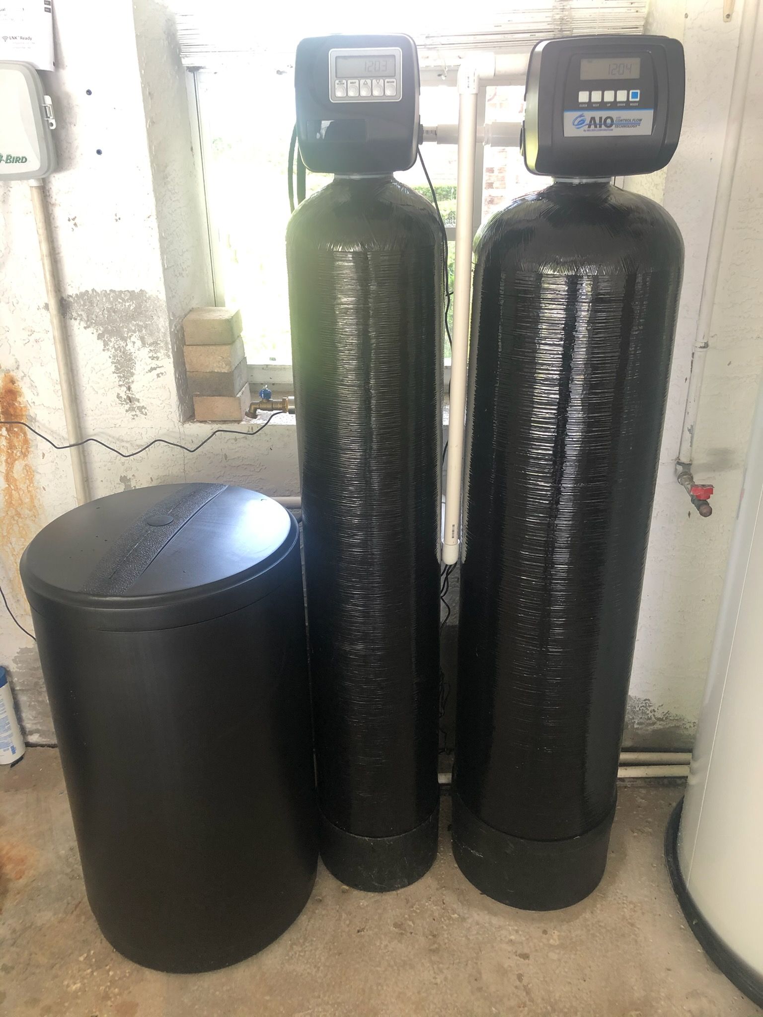Water softener system: two tall black tanks with digital displays, a cylindrical salt tank.