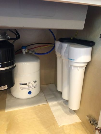 Under-sink reverse osmosis water filter system with three filter cartridges and a storage tank.