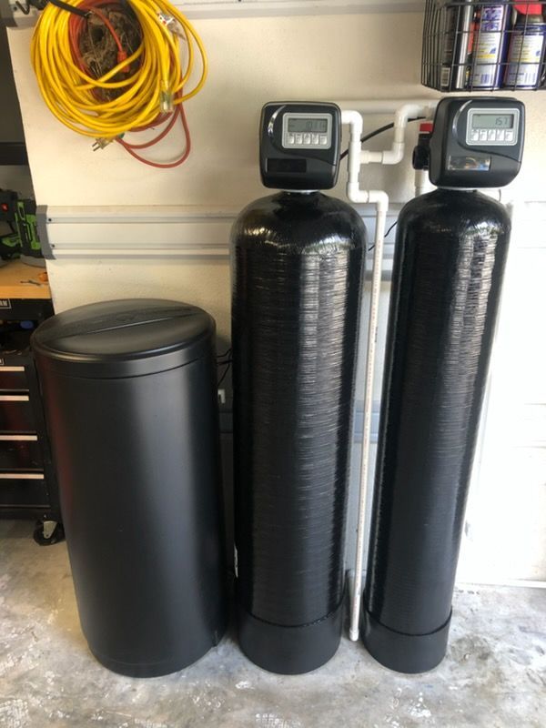 Water softening system with a brine tank and two tall black tanks against a white wall in a garage.