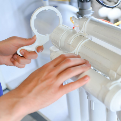 Hands holding wrench, adjusting water filter system.