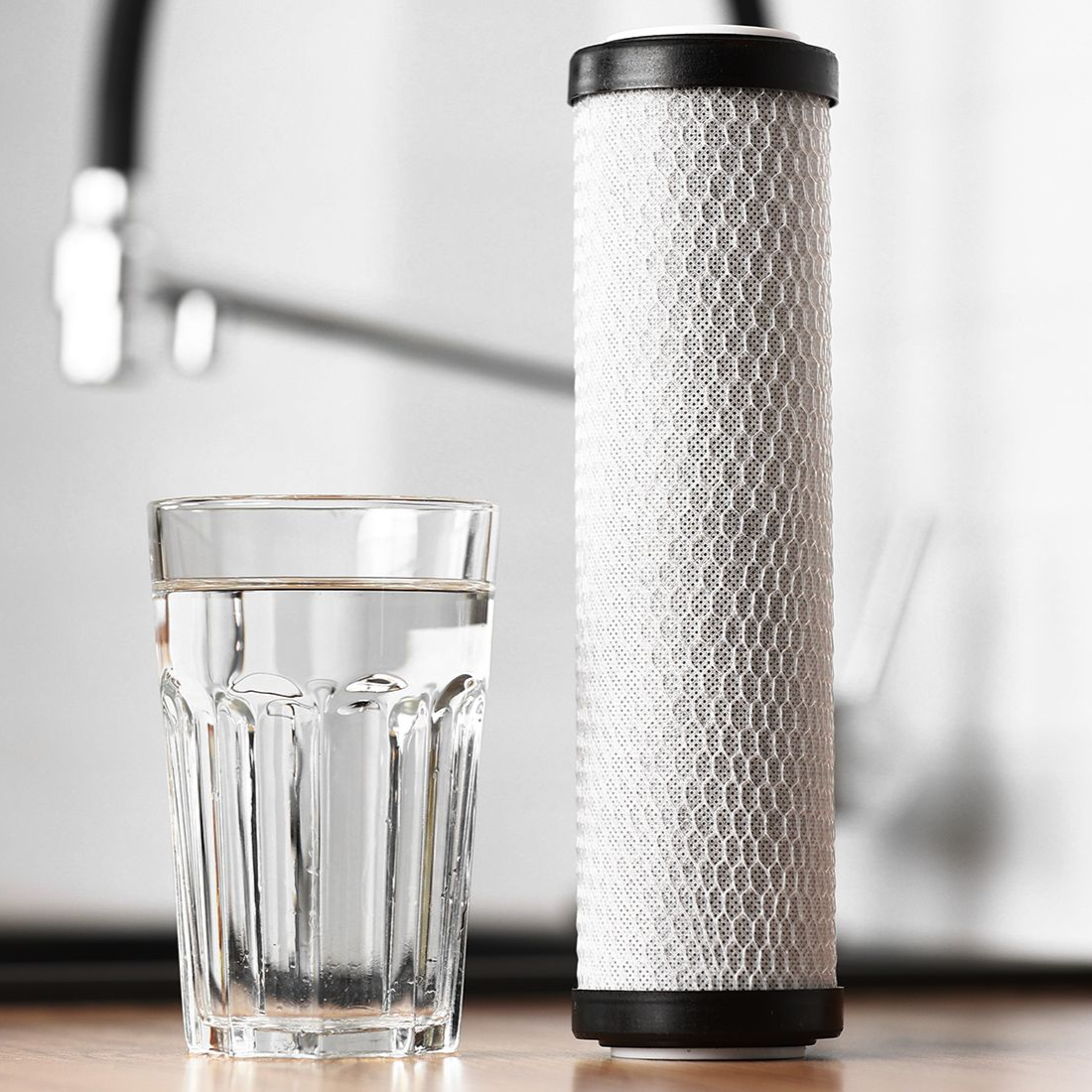 Glass of water next to a cylindrical water filter, next to a sink.