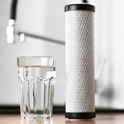 Glass of water next to a cylindrical water filter, next to a sink.
