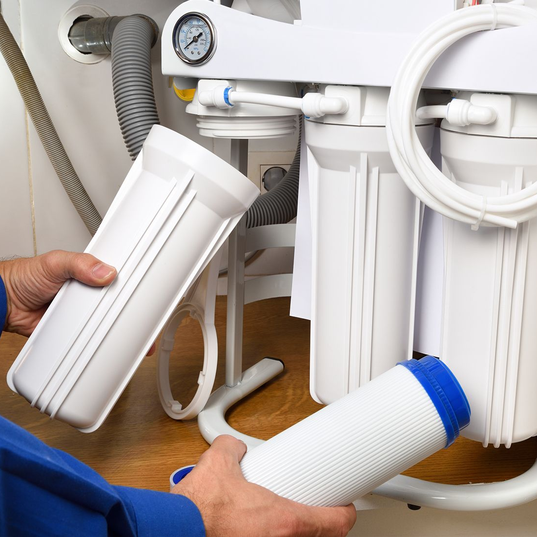 Person changing water filter cartridges under a sink; white cartridges and filter system.