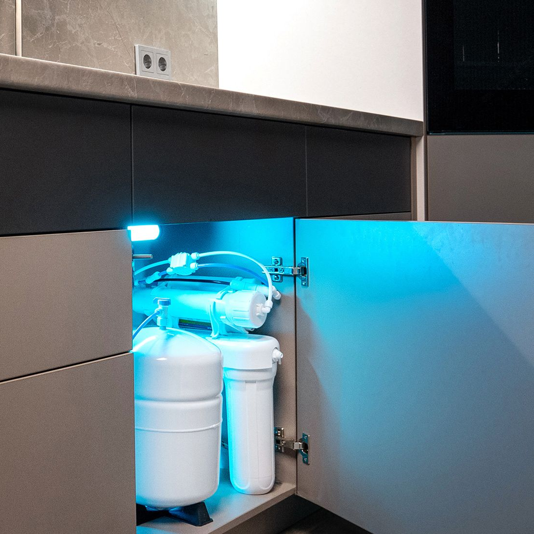 Water filter system installed in a kitchen cabinet with blue lighting.
