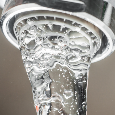 Close-up of a chrome faucet with water flowing, filled with air bubbles, against a light background.