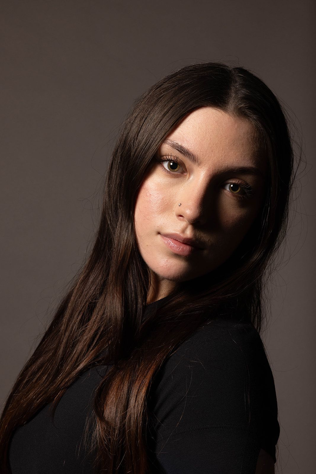 A person with long, dark hair wearing a black top, captured in a studio portrait with dramatic side lighting.