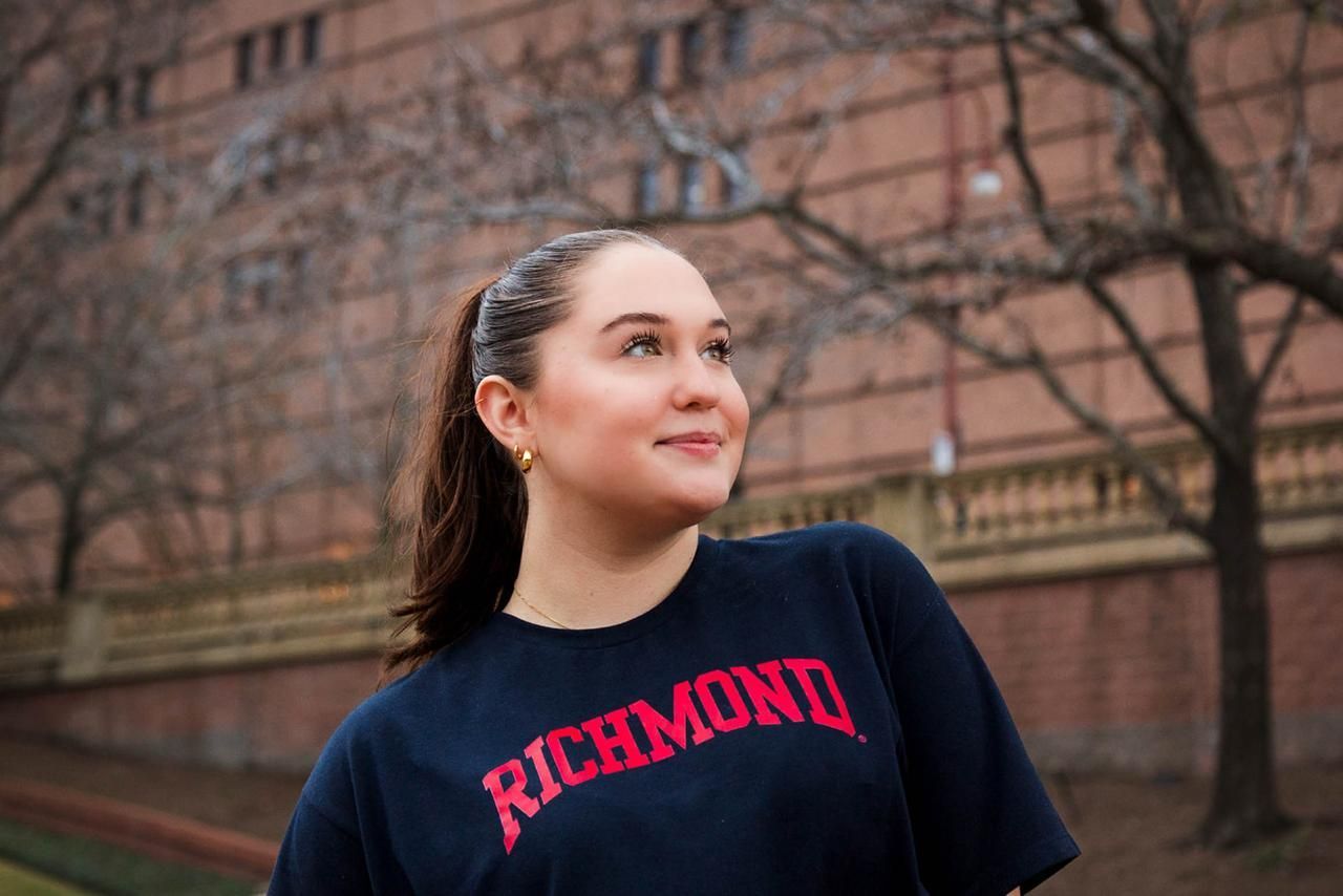 Two people standing back-to-back in a park, both smiling, surrounded by trees and greenery.