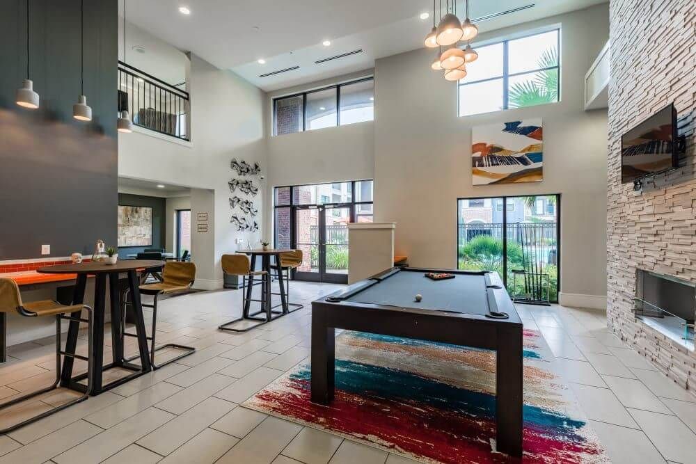 Spacious apartment lounge with a pool table, bar seating, large windows, and decorative artwork.