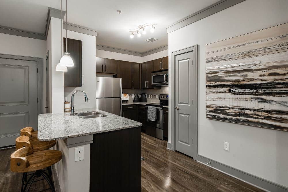Kitchen with granite island, brown cabinets, stainless steel appliances, and wood flooring.