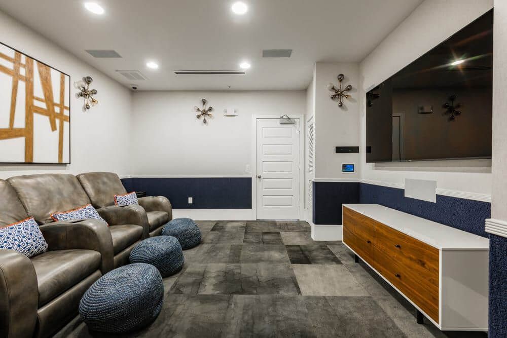 A home theater with leather recliners, a large TV, blue and gold accents, and patterned carpet.