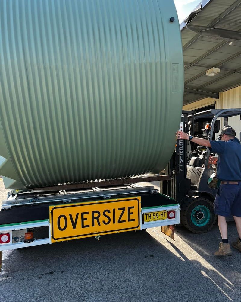 A Large Green Water Tank is Loaded Onto a Trailer by a Forklift — Gloucester Rural Supplies in Stroud, NSW