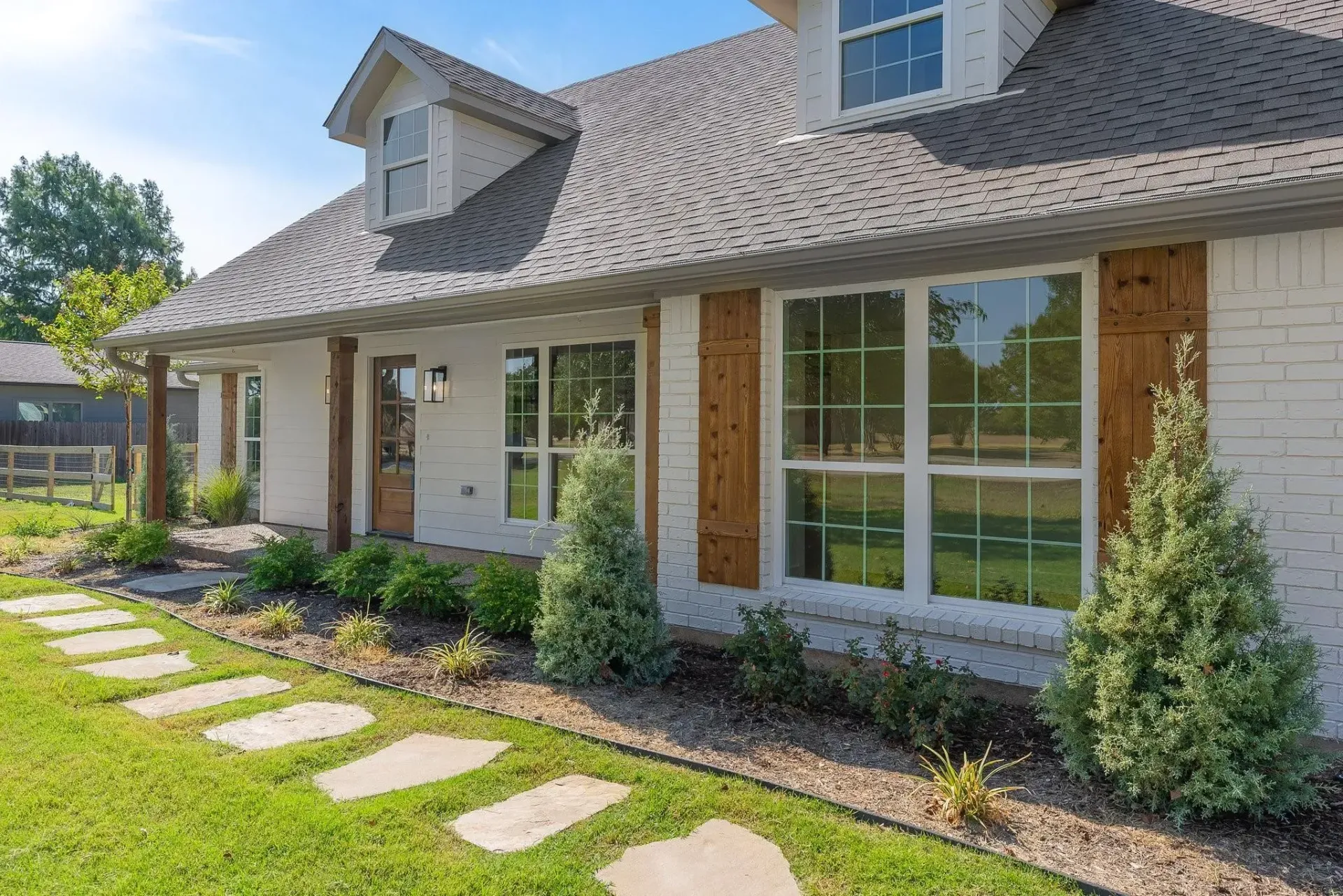 A white brick house with a gray roof and a walkway leading to it.