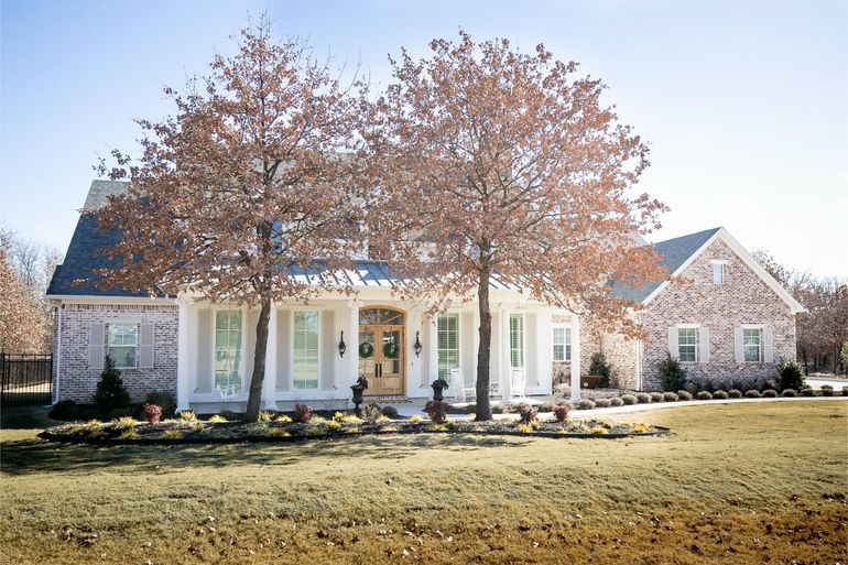 A large white house with a porch and trees in front of it.