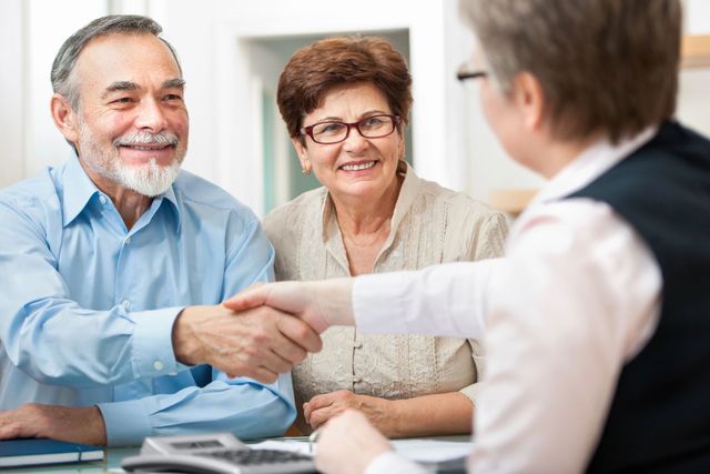 An elderly couple is shaking hands with a woman while sitting at a table.