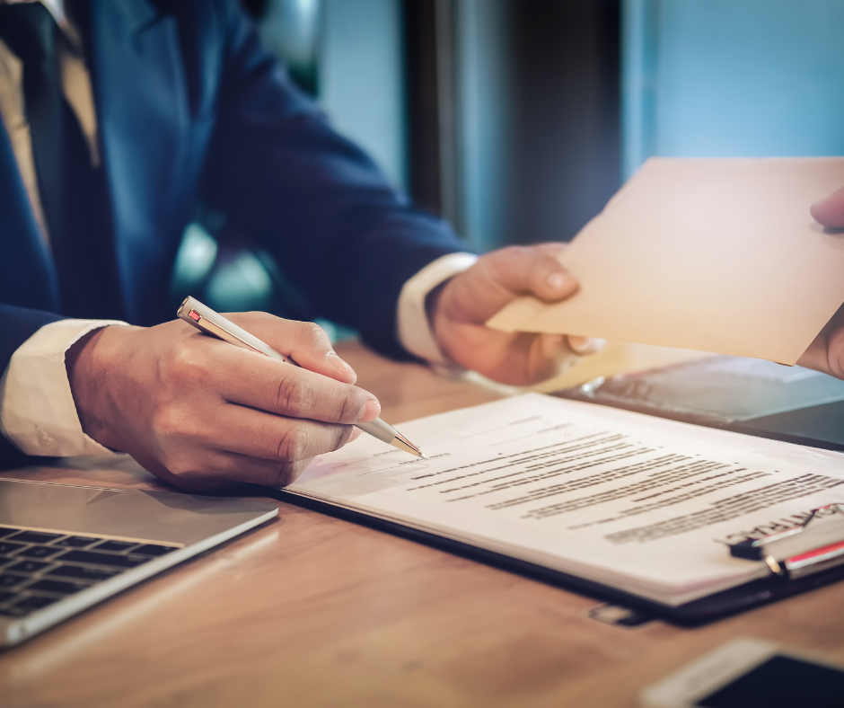 A man in a suit is writing on a piece of paper with a pen.