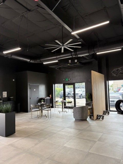 Modern, dark-walled interior of a business. Reception area with tables, a large fan, and an outdoor view.