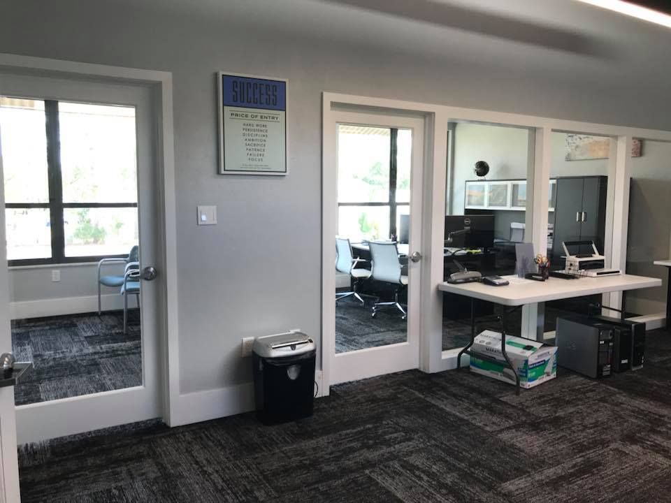 A room with a desk , chairs and a trash can in it.