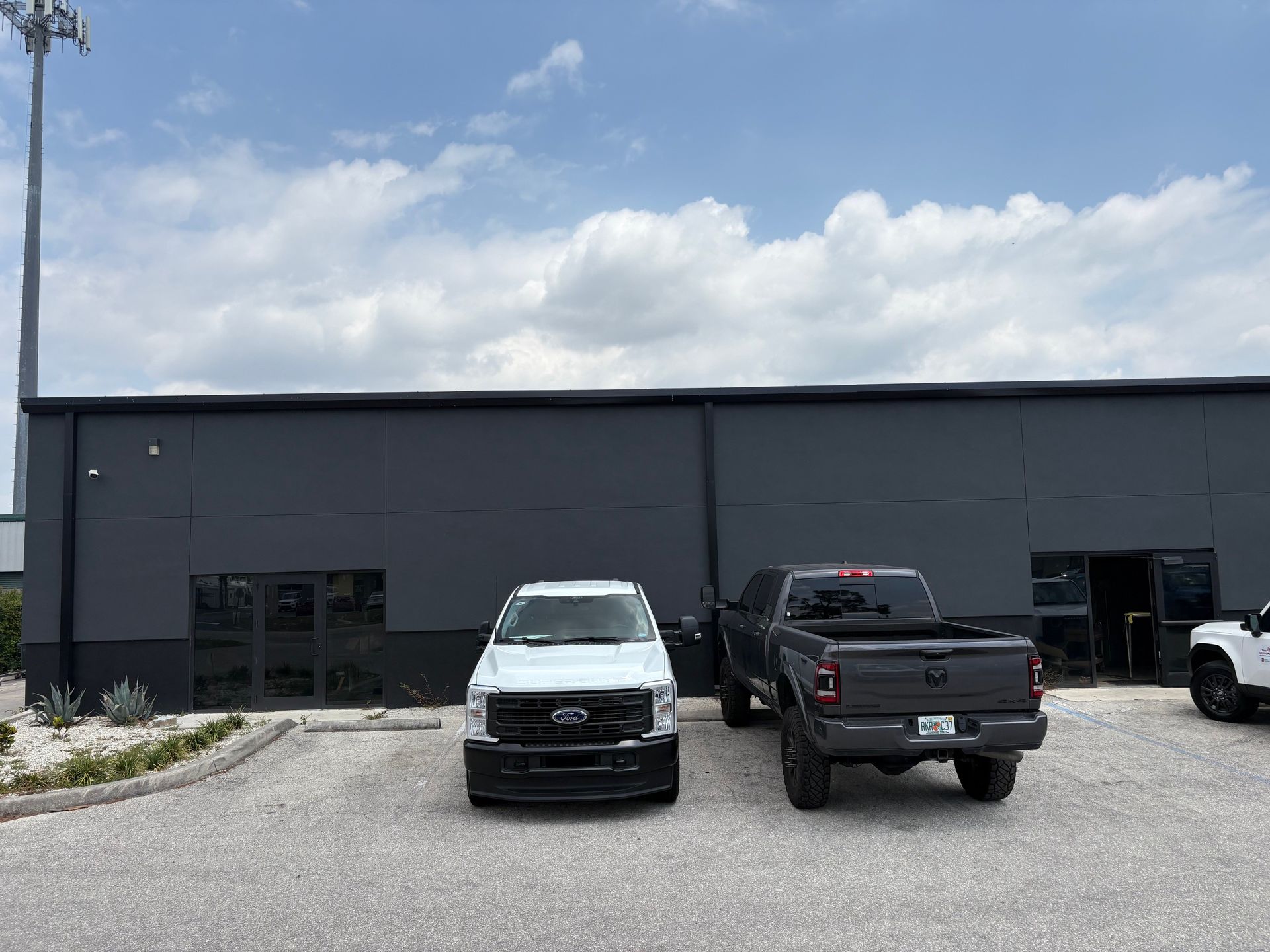 Gray building with three trucks parked out front under a partly cloudy sky.