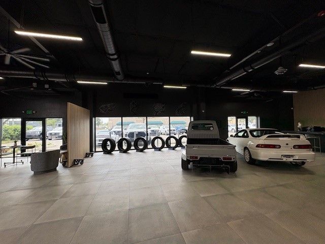 A modern showroom with a mini truck, white car, tires, and windows showing cars outside.