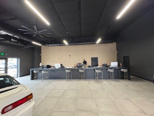 Interior of a modern car showroom with a long counter, staff, and a sports car in the foreground.