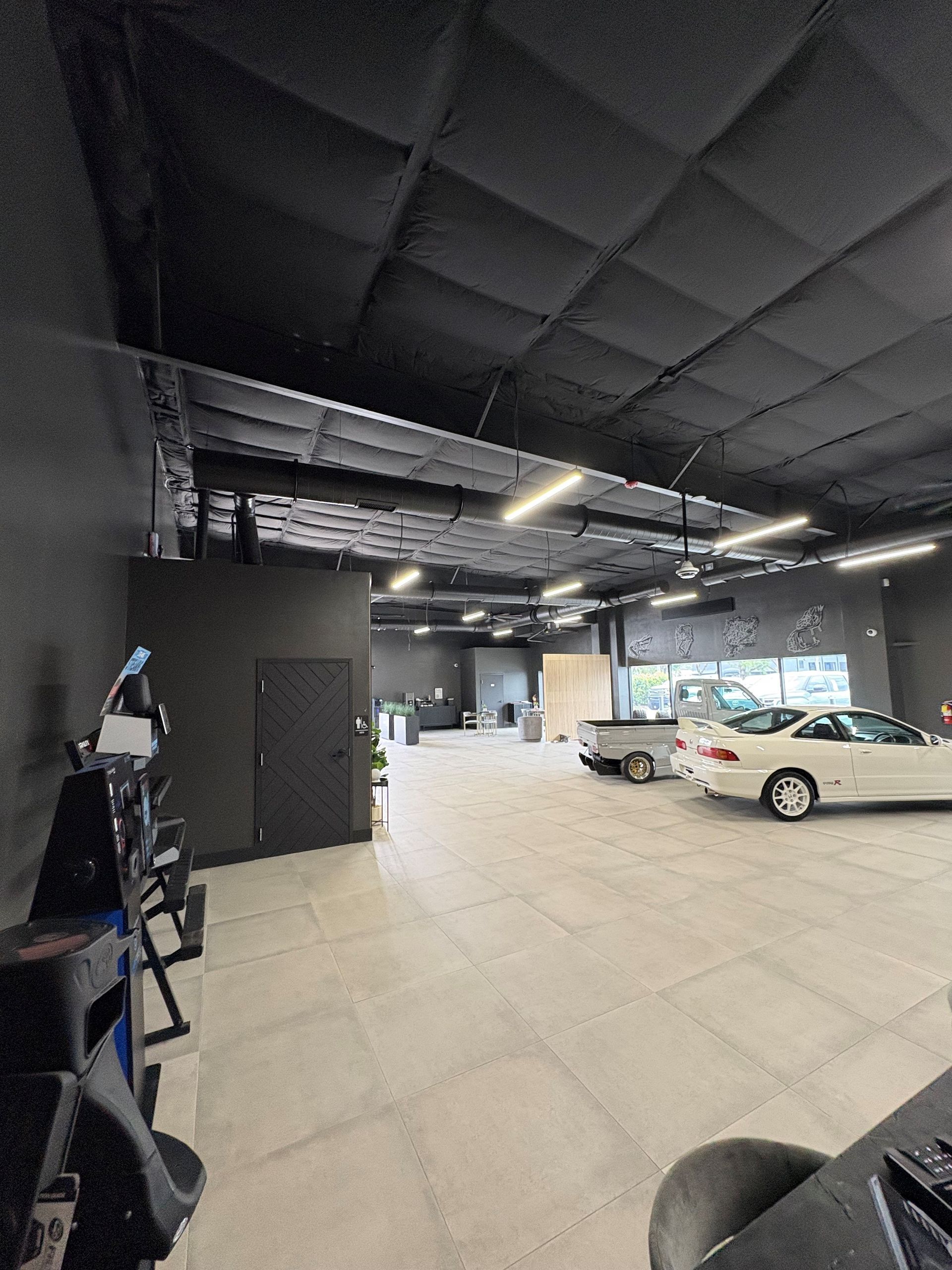 Interior view of a car dealership, featuring a black ceiling and gray tiled floors, with cars on display.