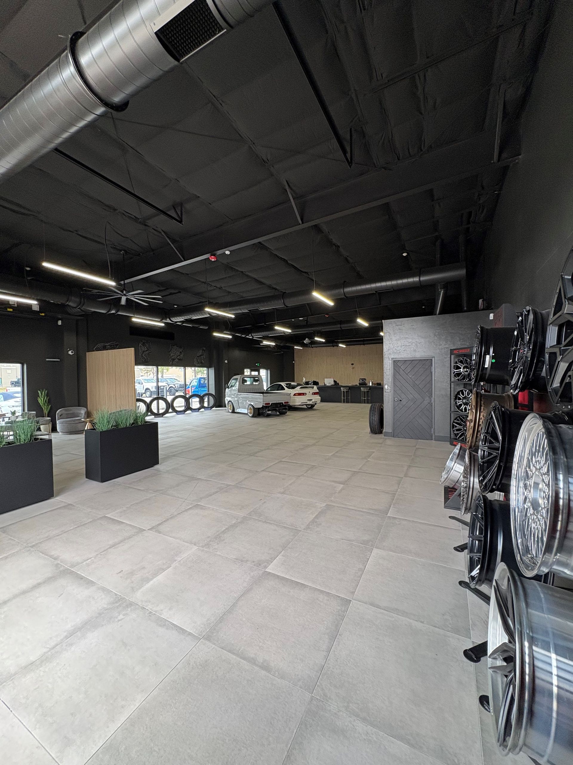 Interior of a car shop, with a car in the center, wheels on the right, and a gray floor.