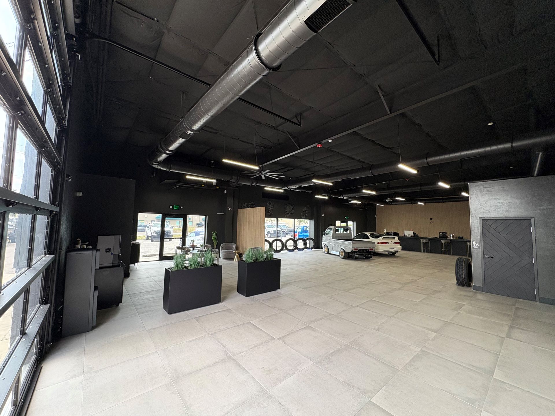 Spacious, modern showroom with black ceiling and walls, large windows, tiled floor, and a few vehicles.