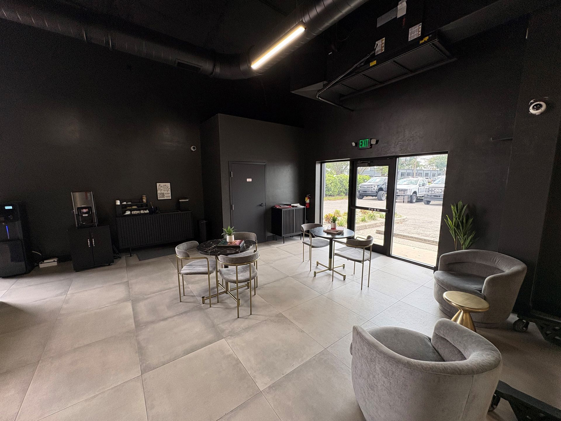 A modern, black-walled event space with seating and tables, a doorway, and a view to the outside.