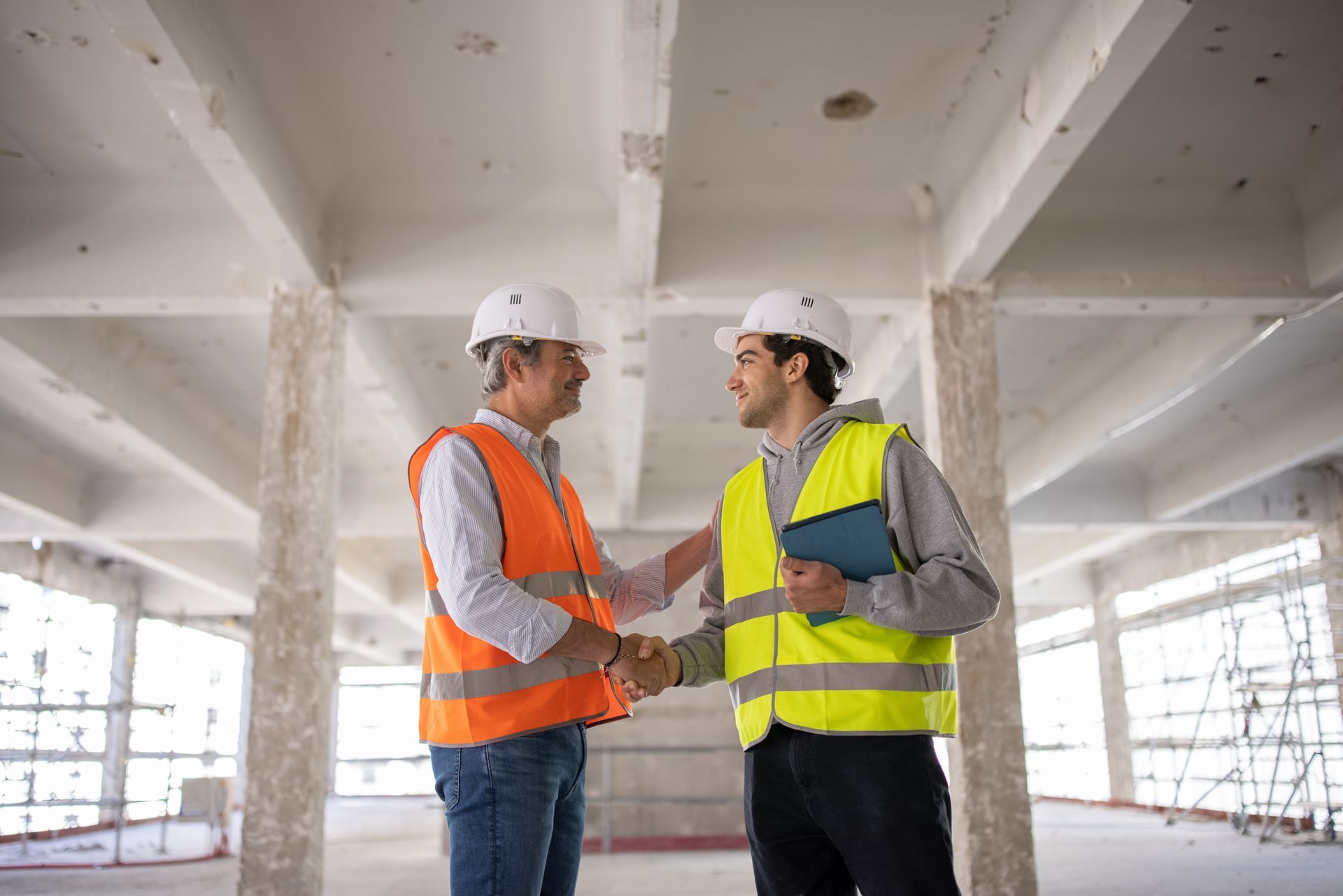 Two commercial renovation contractors, in protective gear, are shaking hands at a construction site.