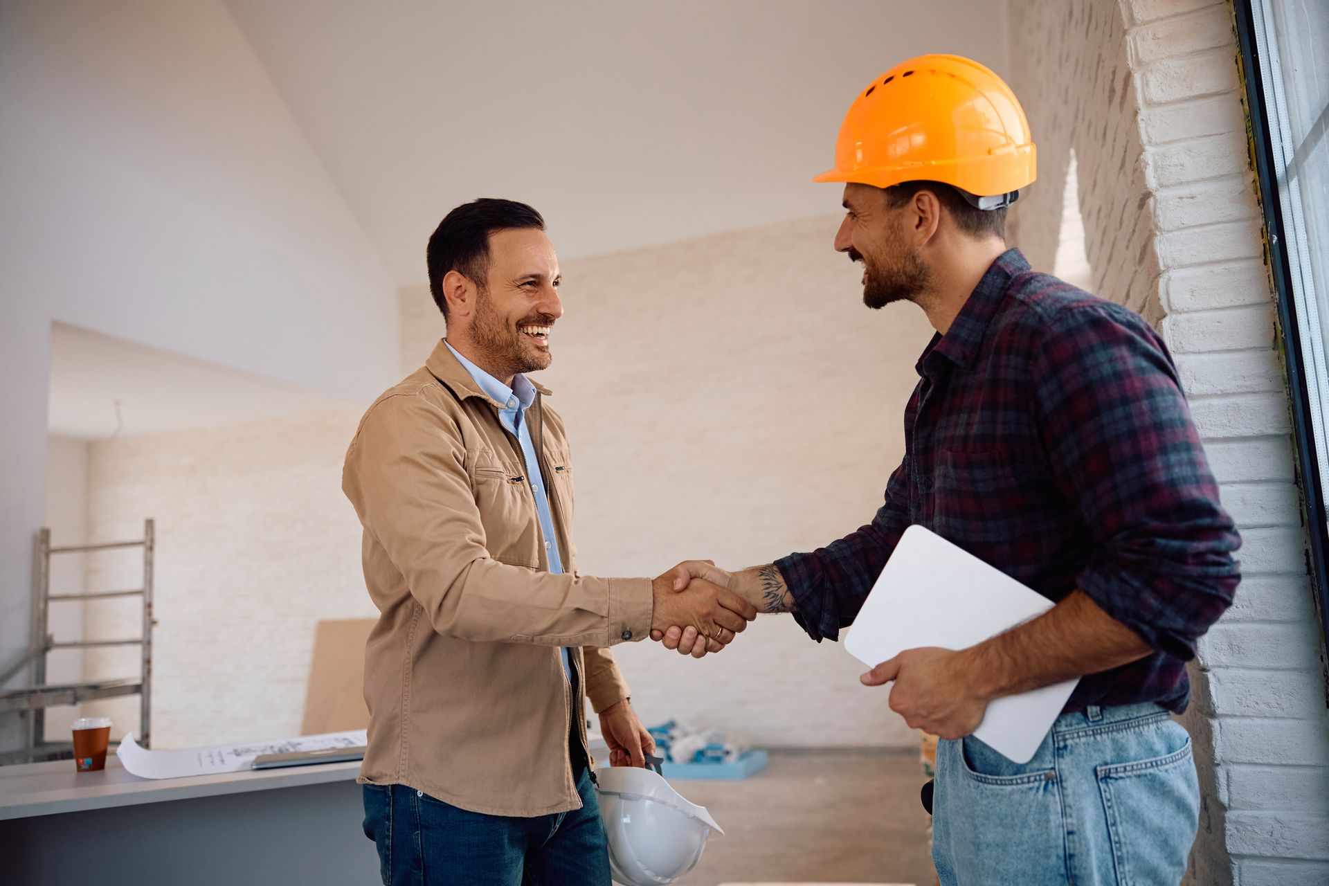 Two men shaking hands at construction site, one wearing a hard hat.