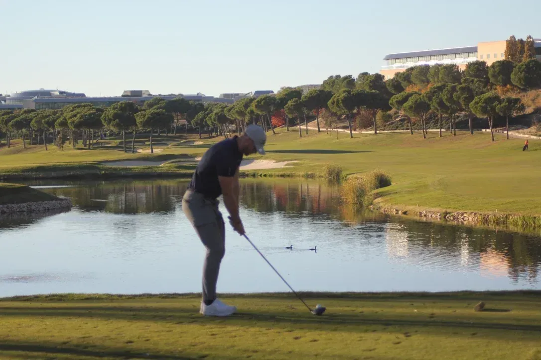 Golfspiller tar en sving på en tee, nær vannhinder.