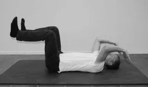 Person som ligger på ryggen på en matte, med beina hevet og armene bøyd over hodet.