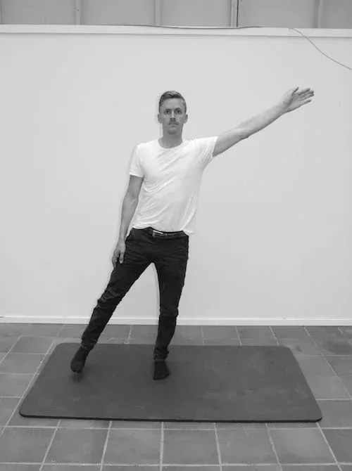 Mann står på en matte, med venstre ben og høyre arm utstrakt, og øver på balanse.