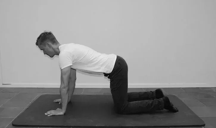 Person i firbenet stilling på en matte, som utfører en kjernemuskulaturøvelse.
