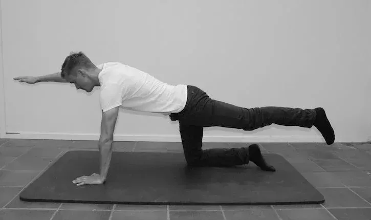 Mann på matte i bordposisjon, strekker ut høyre ben og venstre arm, øver pilates.