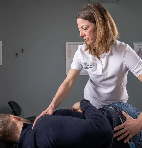 En helsepersonell hjelper en pasient som ligger på et bord, sannsynligvis for fysioterapi.