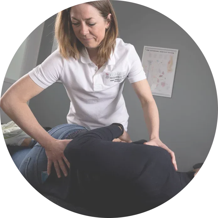 Kvinne i hvit skjorte gir ryggmassasje på en massasjebenk.