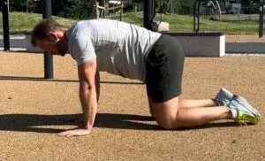 Person på hender og knær, gjør en øvelse utendørs.