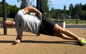 Mann gjør en sideplanke utendørs, støtter kroppen på underarm og fot, den andre armen på hoften.