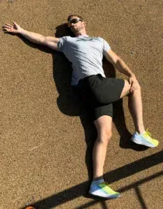 Mann liggende på bakken, utfører en spinal vridningsstrekk, arm utstrakt, ben bøyd.