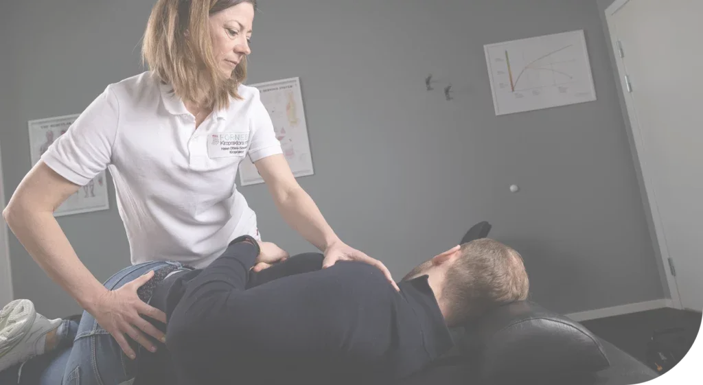 Kvinne i hvit skjorte hjelper en annen person som ligger på et terapibenk i et rom.
