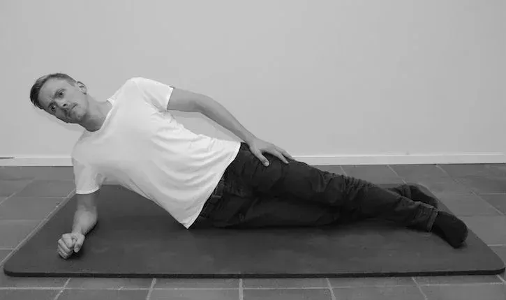 Mann i hvit skjorte og jeans gjør sideplanke på en matte.