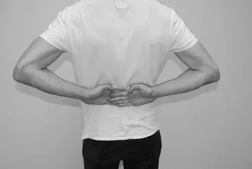 Person med armene bak ryggen, hendene foldet nær livet, iført en hvit t-skjorte.