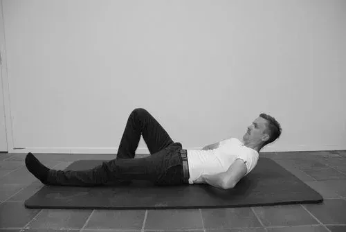 Mann ligger på ryggen på matten, med bøyde knær, hendene støtter korsryggen.