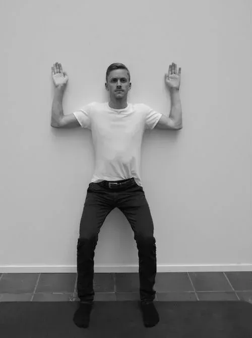 Mann sitter på veggen med hendene hevet mot en hvit vegg.