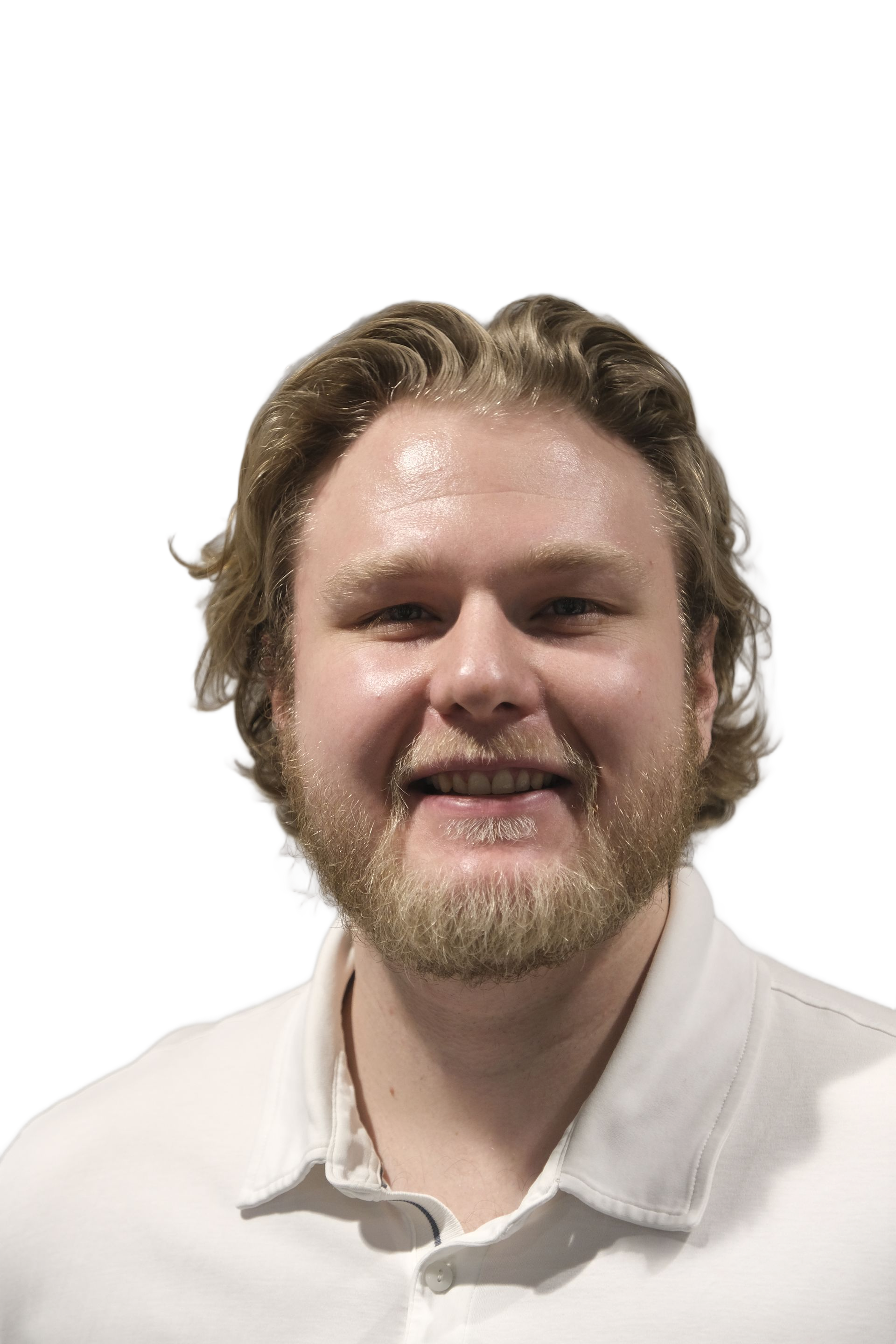 Mann med kort brunt hår og skjegg, iført en hvit poloskjorte, armene bak ryggen, ser på betrakteren.