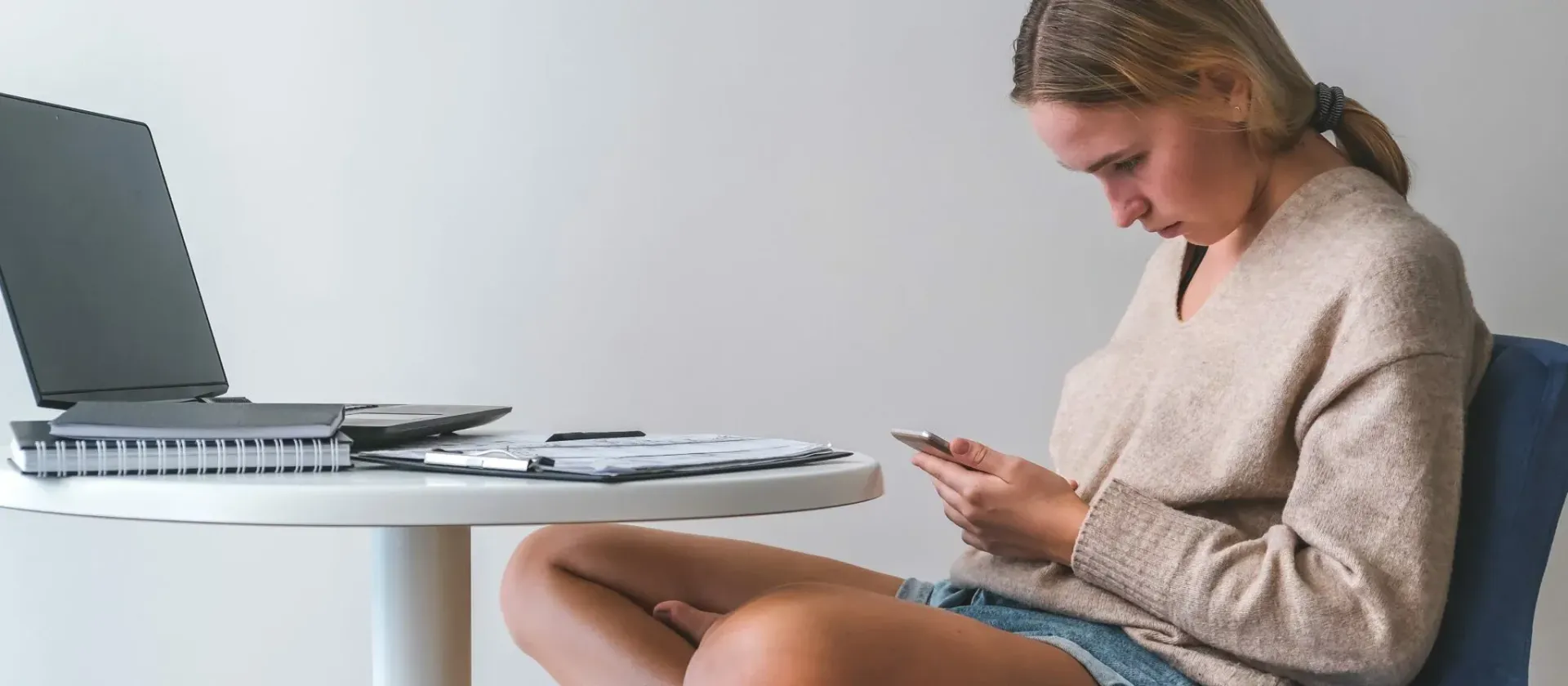 En person sitter ved et bord og ser på en telefon mens deler til en bærbar PC ligger spredt utover.