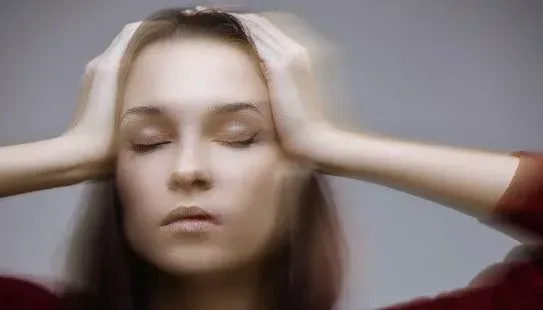 Kvinne med lukkede øyne, hendene på hodet, uskarp effekt som antyder hodepine eller stress.